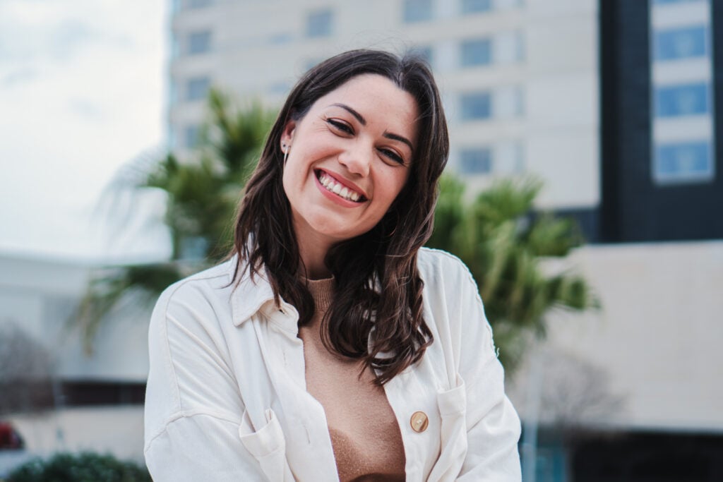 Portrait of young woman smiling and looking at camera with white tooth standing outdoors. Front view of happy teenage girl with positive attitude.