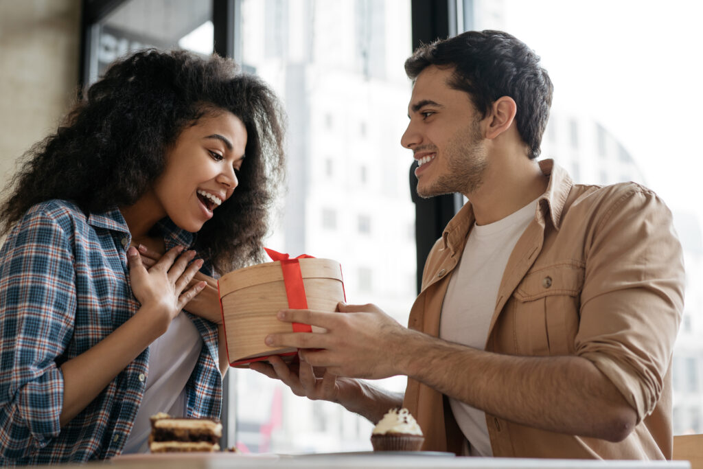 man-giving-birthday-gift-beautiful-woman-multiracial-couple-sitting-together-cafe-dating
